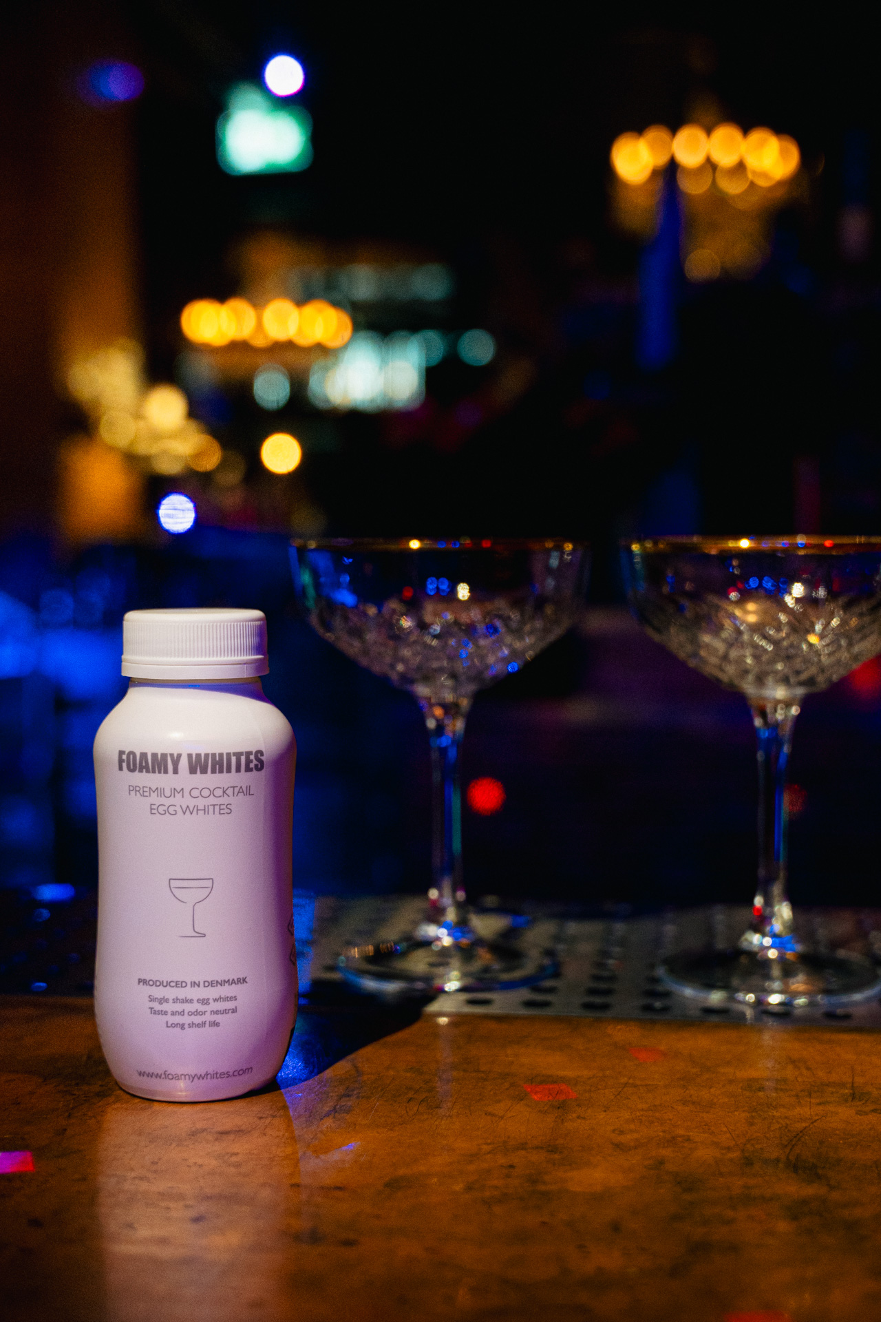 The FOAMY WHITES bottle resting on the bar between coupes.