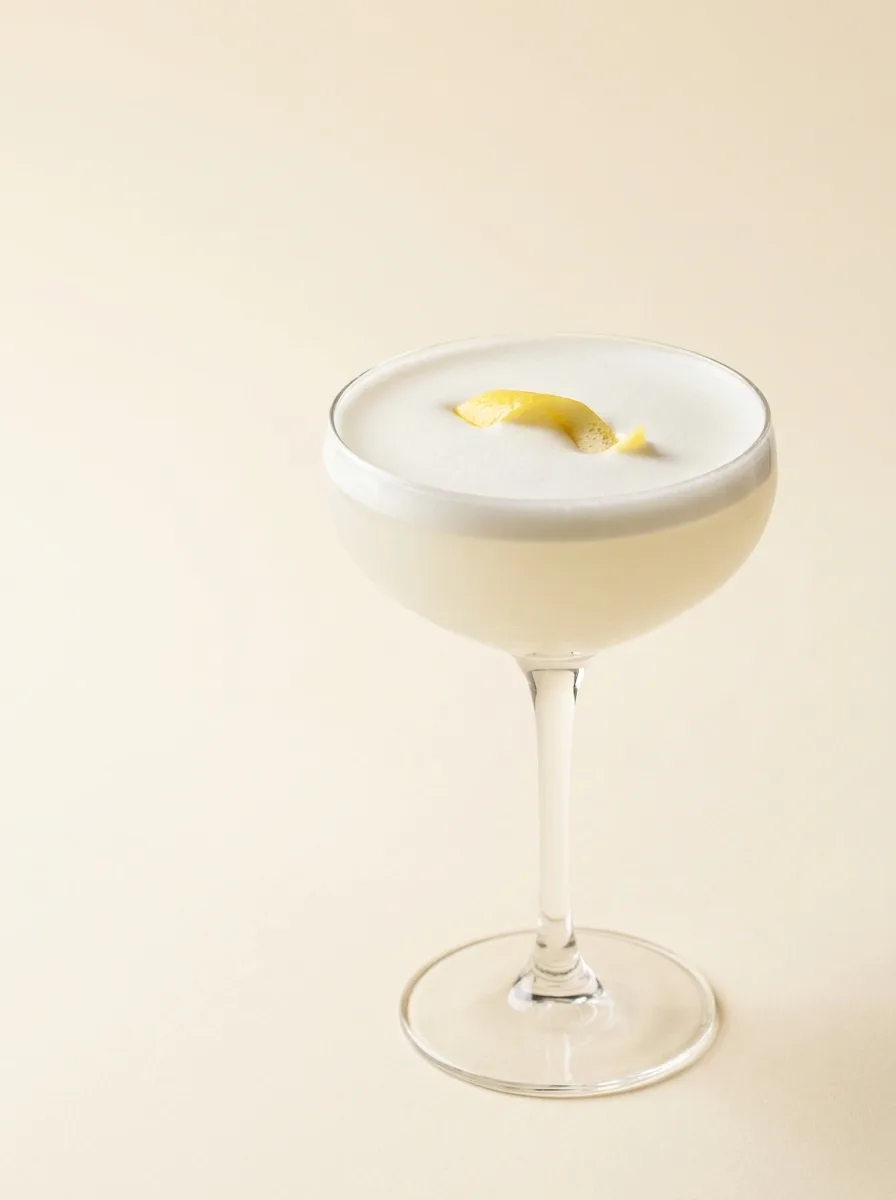 A White Lady cocktail with a silky egg-white foam head, shot in soft editorial light
