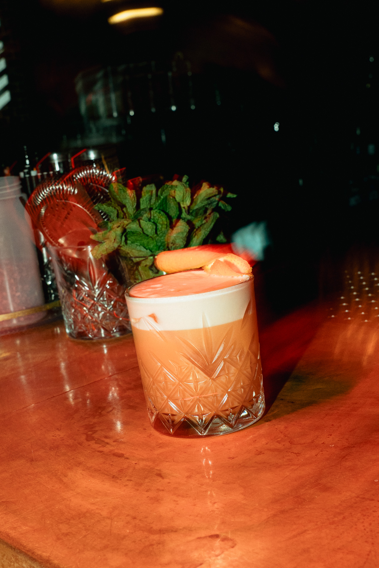 A mint whisky sour on the wood of the bar.