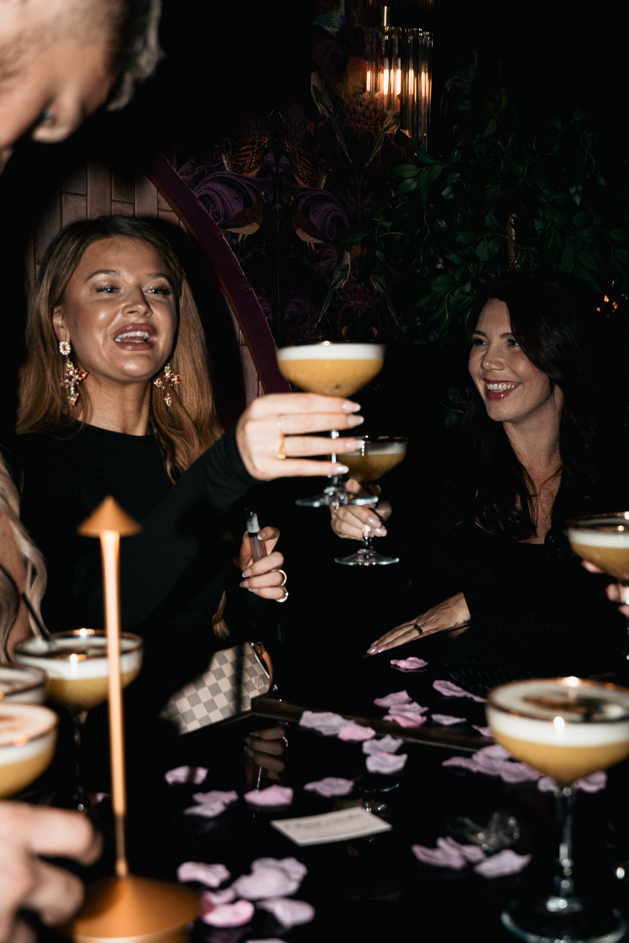 A guest lifts a foam-topped coupe by candlelight.